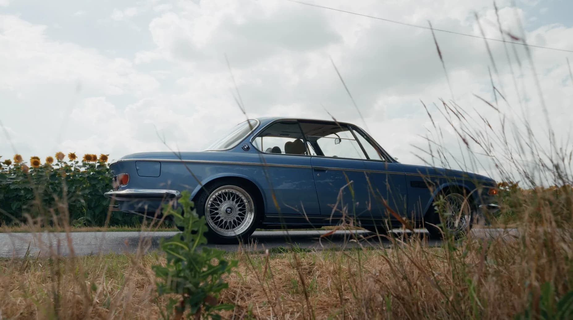 Classic blue BMW driving on the road during a Kárai Exclusive episode