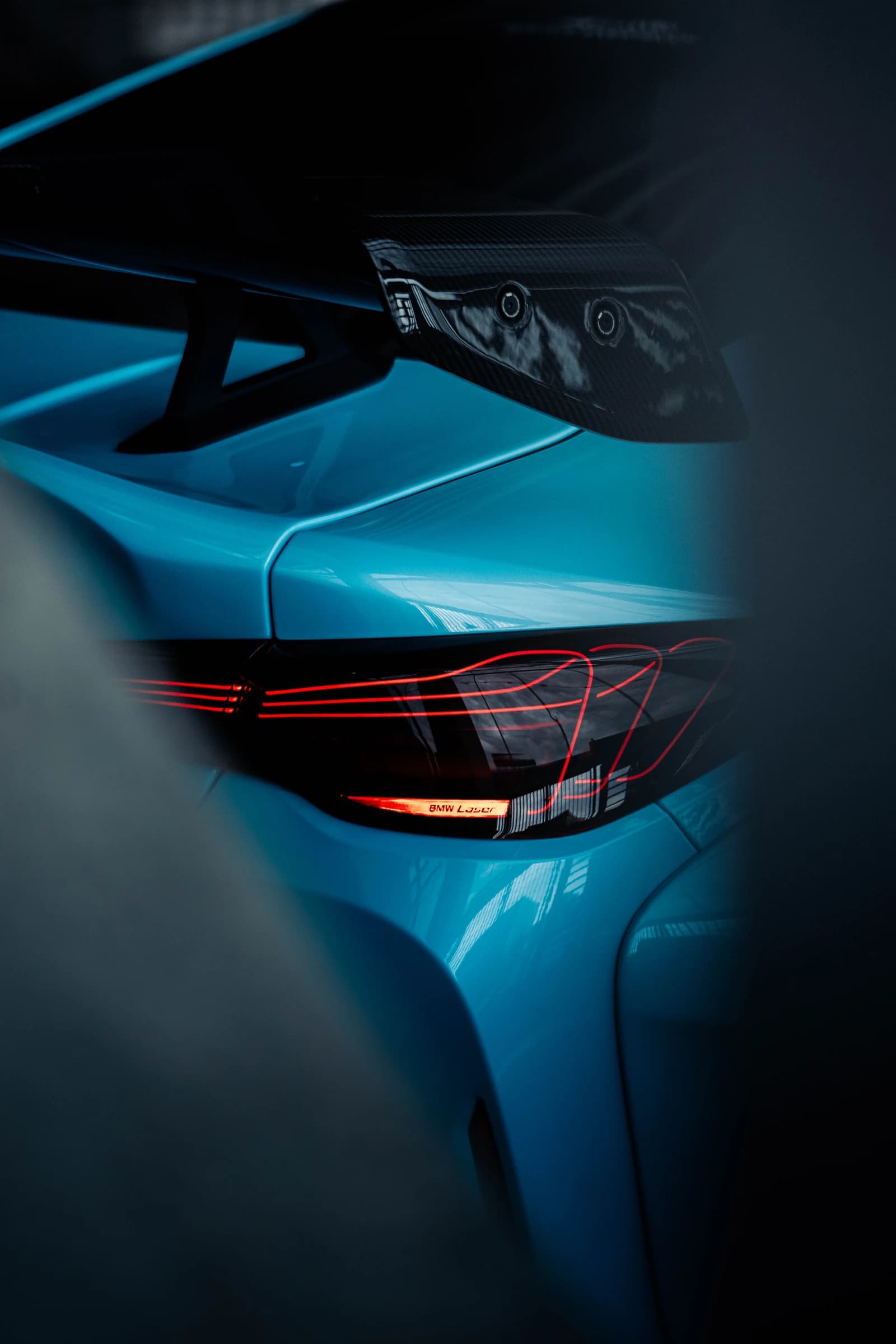 Rear wing and bodywork detail of a turquoise performance car in a darker display area