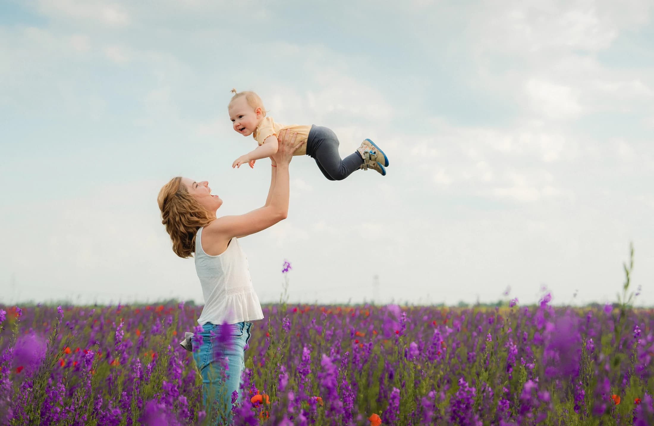 Mother lifting her child against the open sky above a flower field