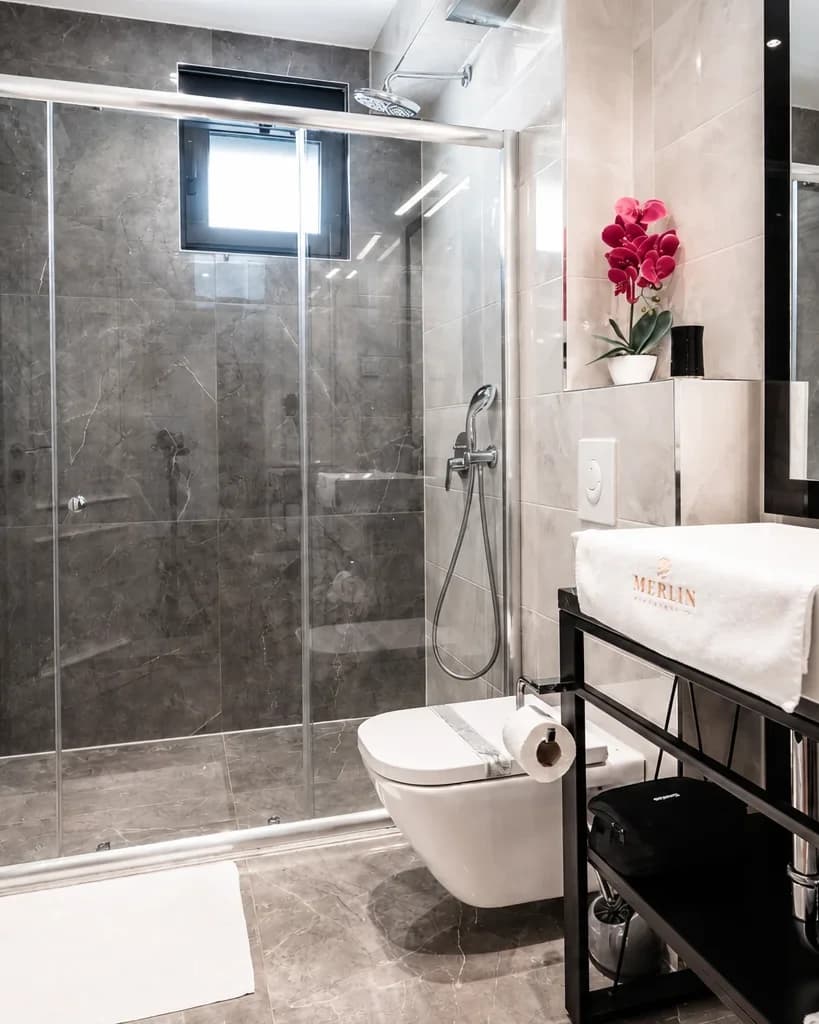 Bathroom at Merlin Apartments with walk-in shower and branded towel