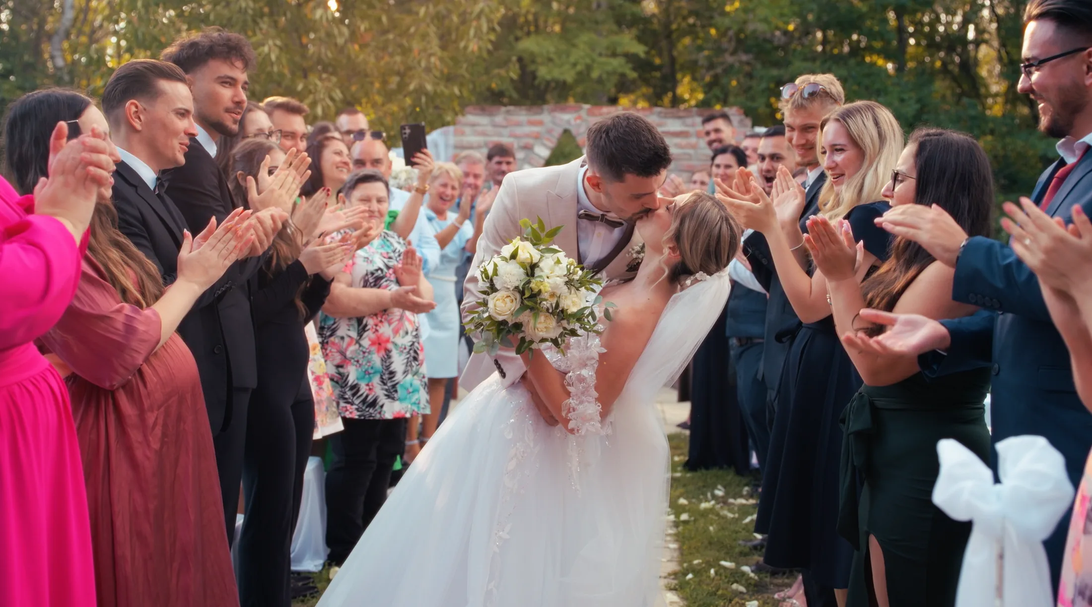 Fanni and Kristóf kissing after the outdoor ceremony as guests celebrate